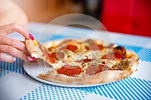 Hand taking pizza slice. Delicious italian pepperoni or salami pizza.