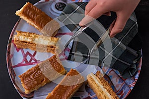 Hand taking traditional Colombian dessert Milhojas with tongs photo