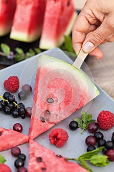 Hand taking watermelon slice on stick from a summer fruits plate