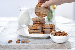 Hand with tasty oatmeal almond cookies with jar of milk on the old marble table beautiful close-up on white background