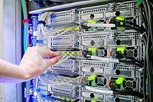 The hand of a technician with a communication Internet wire is a close-up.  Service work in the datacenter server room.