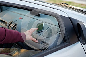 Hand of a thief stealing a mobile phone from a parked car