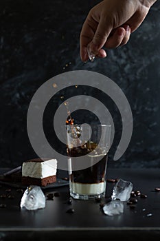 Hand throw a piece of ice into the glass with traditional vietnamese coffee. Souffle dessert and iced coffee. Splash