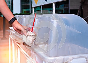 Hand throwing empty plastic coffee cup into the recycling bin