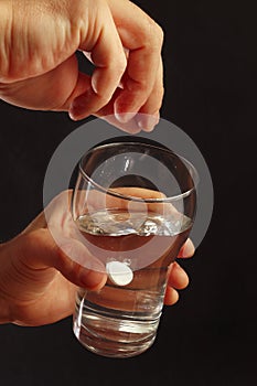 Hand throwing a soluble pill in a glass of water on dark background.