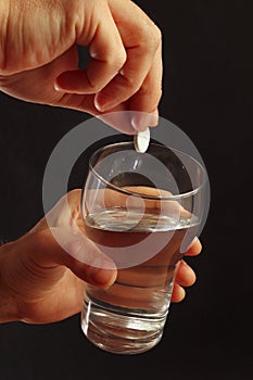 Hand throwing a soluble tablet in a glass of water on dark background.