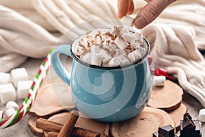 Hand throws marshmallow in a mug of hot chocolate on a wooden background. Cozy warm winter composition