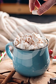 Hand throws marshmallow in a mug of hot chocolate on a wooden background. Cozy warm winter composition