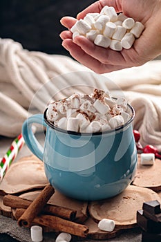 Hand throws marshmallow in a mug of hot chocolate on a wooden background. Cozy warm winter composition