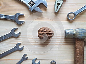 Hand, tool and big walnut on wooden background. The concept of complex problems, the challenge can be solved.