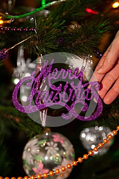 Hand touches inscription Merry Christmas on tree decorated with toys