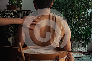 Hand touching a half-naked male next to a wooden Bombo drum at home garden