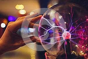 Hand touching a plasma ball with smooth magenta-blue flames.