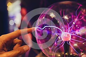 Hand touching a plasma ball with smooth magenta-blue flames.