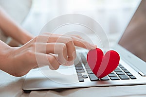 Hand touching red heart on laptop keyboard for flirt love chat or lover online text messenger for find date couple during stay