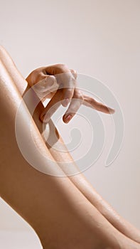 Hand touching smooth moisturized leg in soft warm studio lighting.