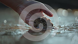 Hand touching the surface of water and holding sand in river at the morning time with sunlight.