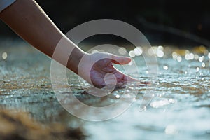 Hand touching the surface of water in the river at the morning time with sunlight.