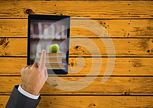 Hand touching tablet showing book pile with apple on yellow table