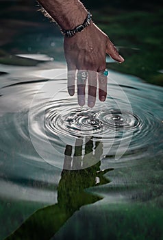 Hand touching the water of the lake, verifying the temperature of the water, the drops of water run down the fingers of the subjec