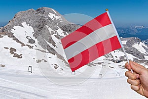 Hand of tourist is holding austria flag in hand. Alps in background.