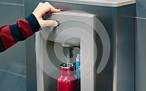 Hand of a traveler pressed the button of drinking water filling station at the Airport photo