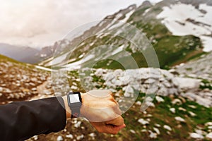 Hand traveler wearing and looking at the smart watch high in the mountains. Modern technologies