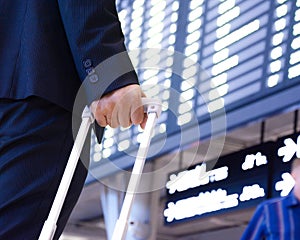 Hand of traveling businessman with baggage in front of airport timetable