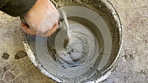 hand with trowel mixing wet cement to prepare the mixture in a bucket