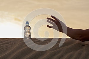 Hand try to catch the bottle of water on sand desert