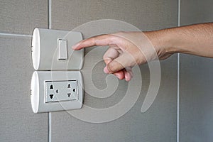 Hand turn on a power, Finger pushing light switch button with plug on ceramic tile wall in bathroom.