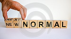 Hand is turning cubes and changes the words `new normal` to `next normal`. Covid-19 postpandemic concept. Beautiful white