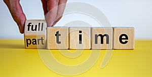 Hand is turning a dice and changes the word `full-time` to `part-time` or vice versa. Beautiful yellow table, white background