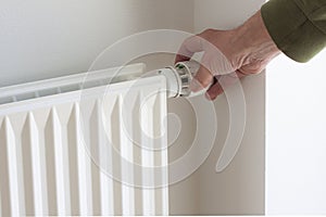 Hand turning down adjusting knob on thermostat on radiator valve to save energy