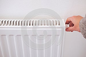 Hand turning down thermostat of a central heating radiator.