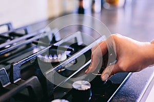 Hand turning on gas burner on kitchen stove top