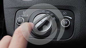A hand turning on headlights and fog lights of a modern car, detail of the headlightbutton, light knob