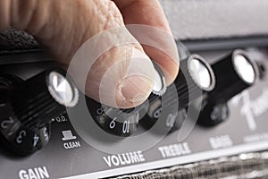Hand turning up the volume of a guitar amplifier, treble and bass control knobs out of focus , equalization dials close up photo
