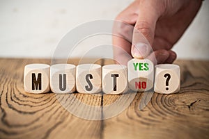 Hand is turning wooden cube with yes an no answer to the question MUST?
