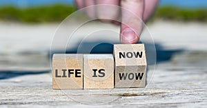 Hand turns cube and changes the expression 'life is wow' to 'life is now'.