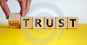 Hand turns a cube and changes the expression `mistrust` to `trust`. Beautiful yellow table, white background, copy space. Busi