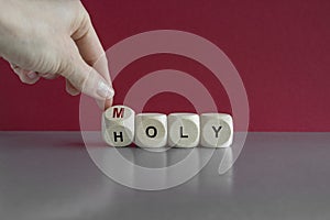 Hand turns a cube and changes the word Holy to Moly. Beautiful green background, gray table. From holy to moly and business