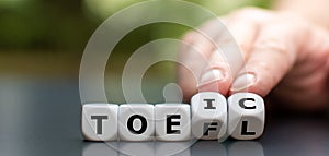 Hand turns dice and changes the acronym `toefl` to `toeic`, or vice versa`. photo