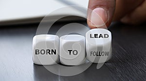 Hand turns dice and changes the expression \'born to follow\' to \'born to lead.