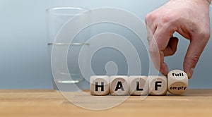 Hand turns a dice and changes the expression `half empty` to `half full`. photo
