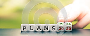 Hand turns dice and changes the expression `plans 2020` to `plans 2021`.