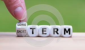 Hand turns a dice and changes the expression `SHORT TERM ` to `LONG TERM ` or vice versa. photo