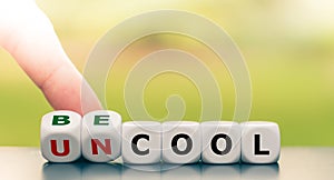 Hand turns a dice and changes the expression `uncool` to `be cool`