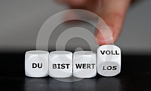 Hand turns dice and changes the German expression `du bist wertlos` you are worthless to `du bist wertvoll`you are valuable