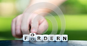 Hand turns dice and changes the German expression `fordern` demand to `foerdern` support.